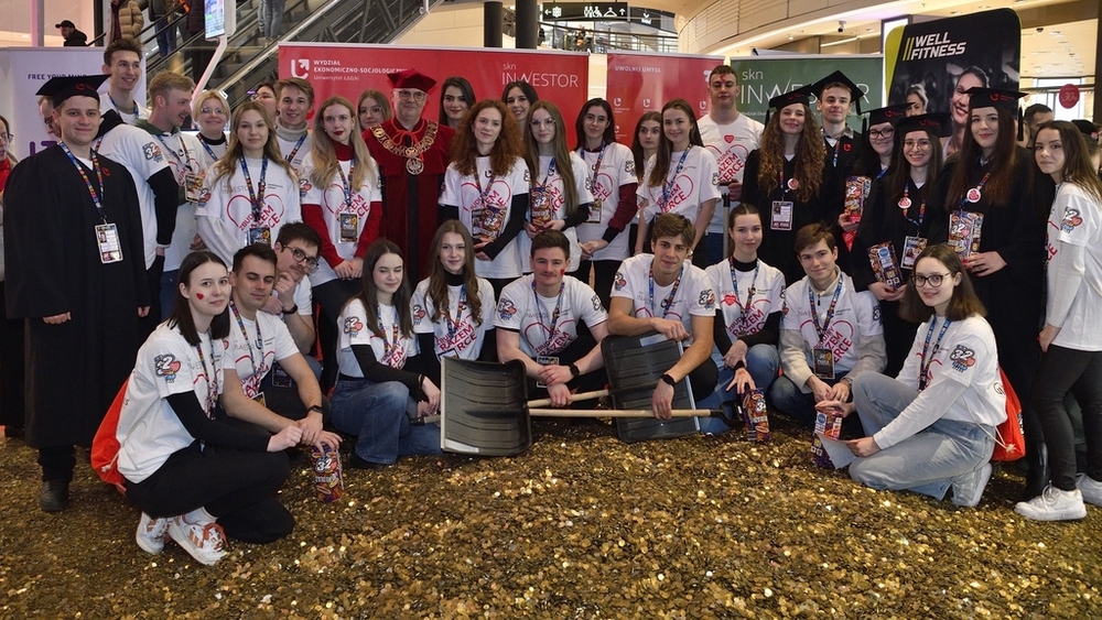 A group of several dozen students standing in front of a large heart made of gold coins