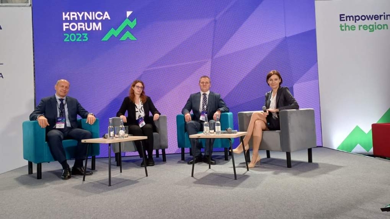 Dwóch mężczyzn i dwie kobiety siedzą przy dwóch stolikach na scenie podczas Forum w Krynicy/Two men and two women are sitting at two tables on the stage during the Forum in Krynica