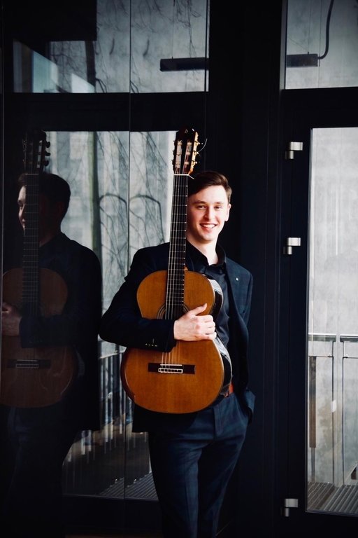 Maksym Niewczas wearing a dark suit and holding a guitar