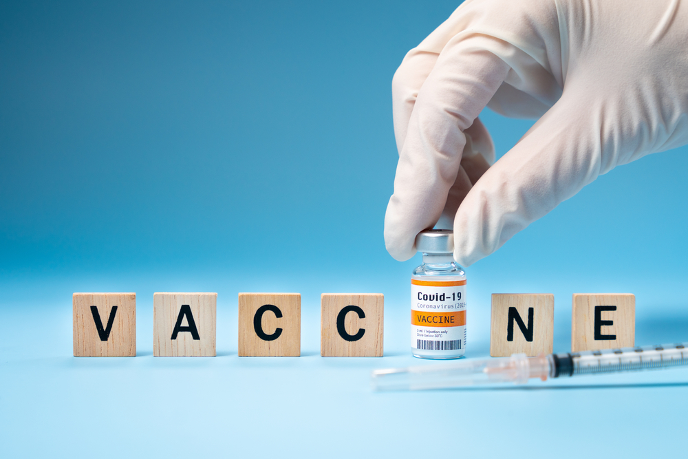 The hand of a researcher in a latex glove takes a vial of 2019-nCov vaccine with wooden letters of the alphabet "VACCINE"