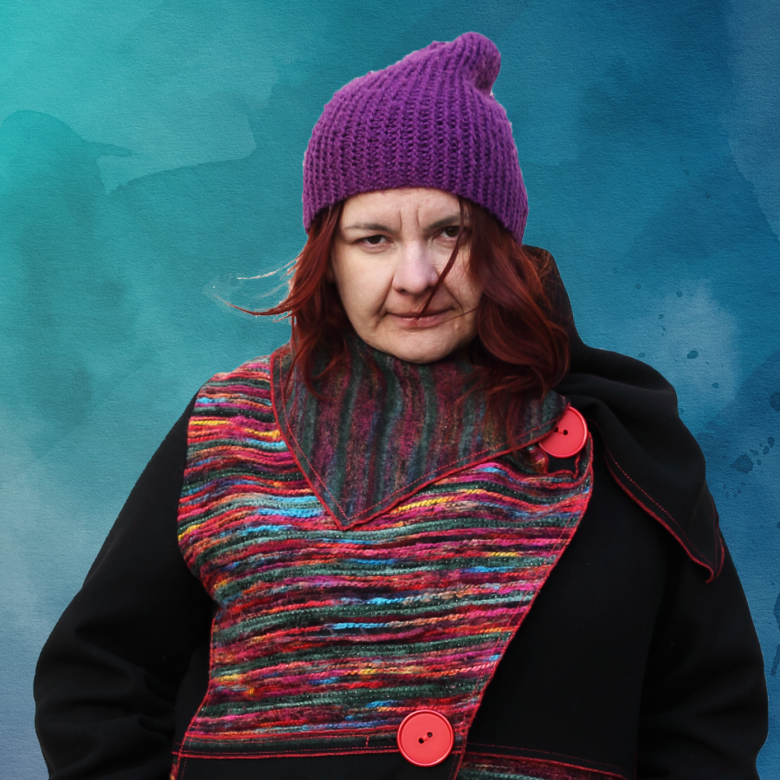 A portrait photo of the winner wearing a coat with colourful parts and a violet hat which compliments her red hair